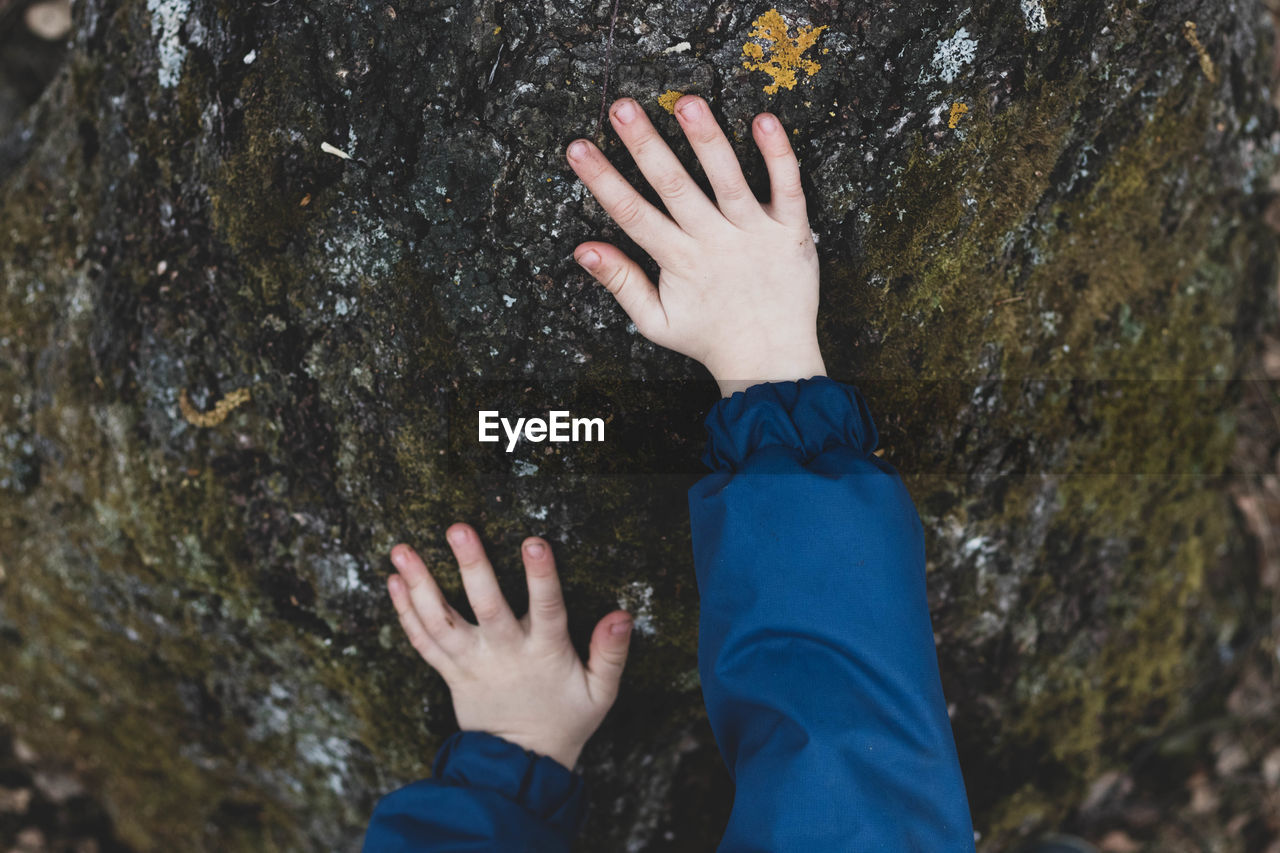 HIGH ANGLE VIEW OF HUMAN HAND TOUCHING ROCK