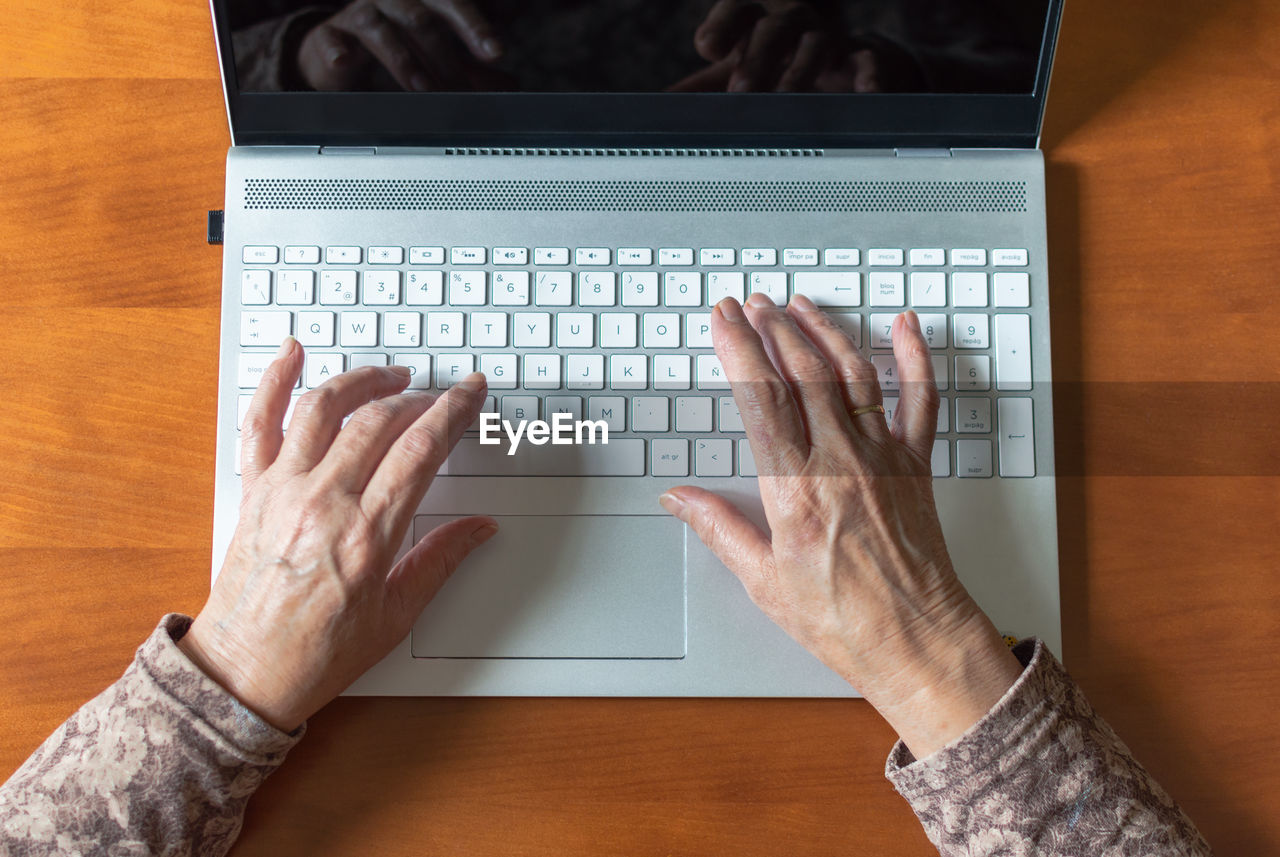Cropped hands of woman using laptop over table