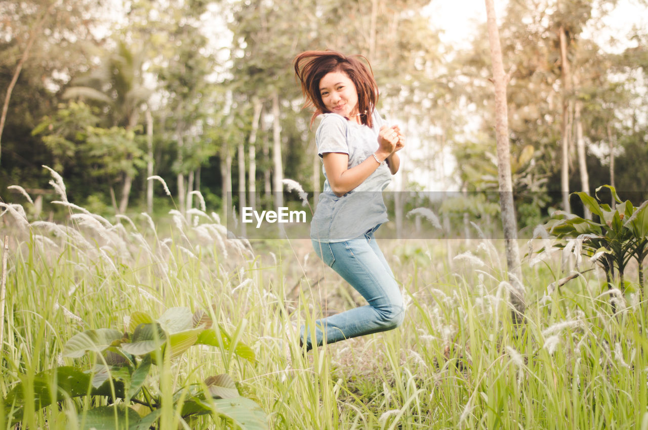 Portrait of smiling woman jumping by plants on field 