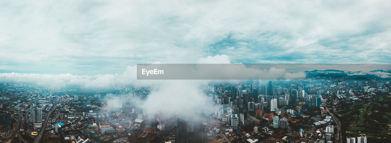 Panoramic view of city buildings against cloudy sky