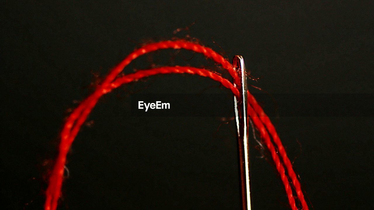 Close-up of red thread going through needle against black background