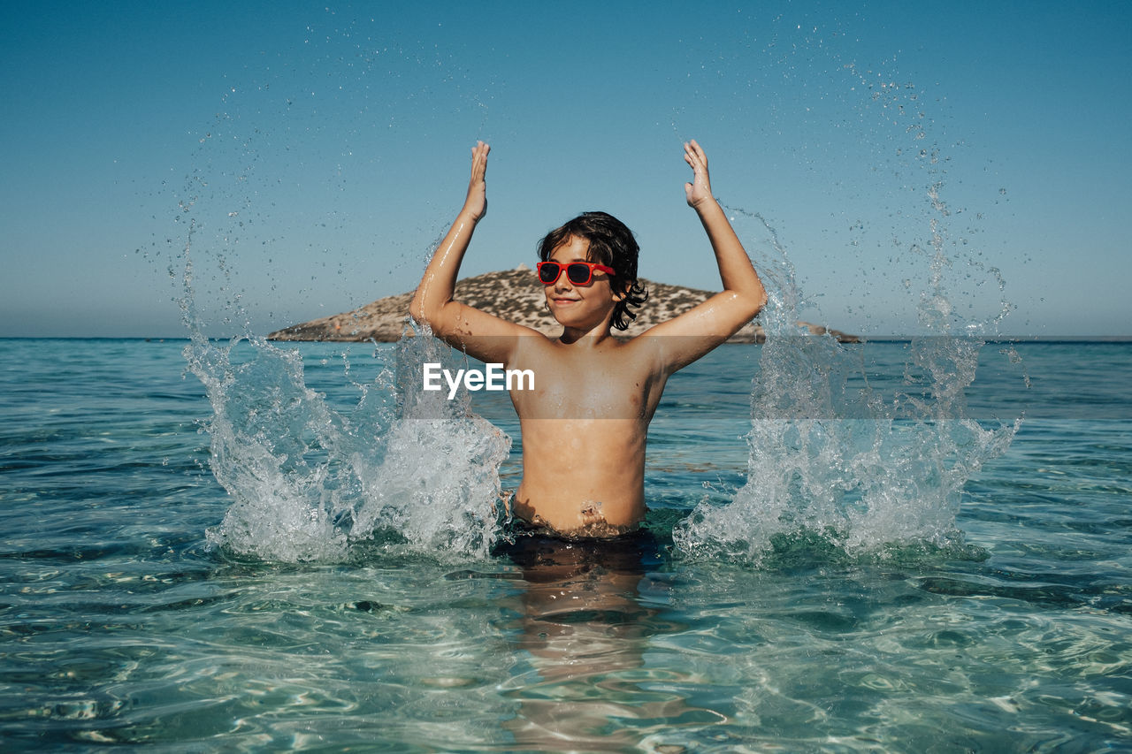 Boy playing with water on the beach in summer while wearing sunglasses