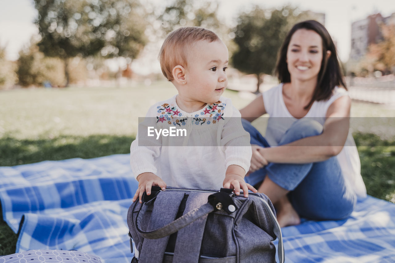 Mother and daughter sitting on picnic blanket at park