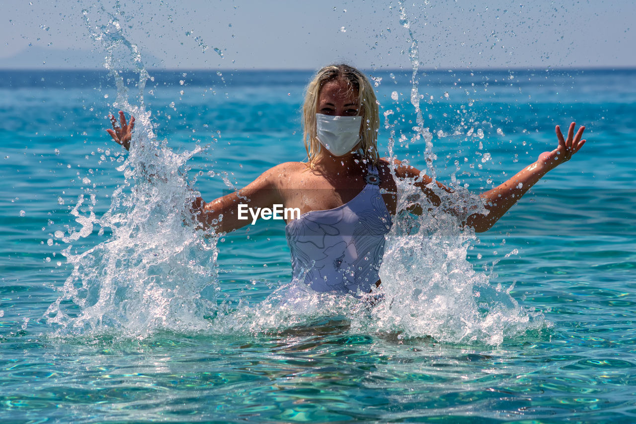 Woman wearing facemask enjoying in swimming pool against sea