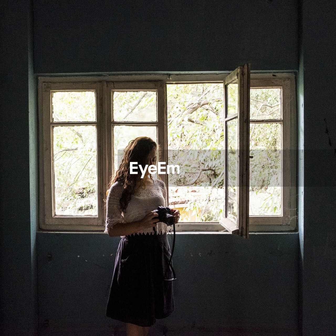 Woman looking at camera while standing by window in room