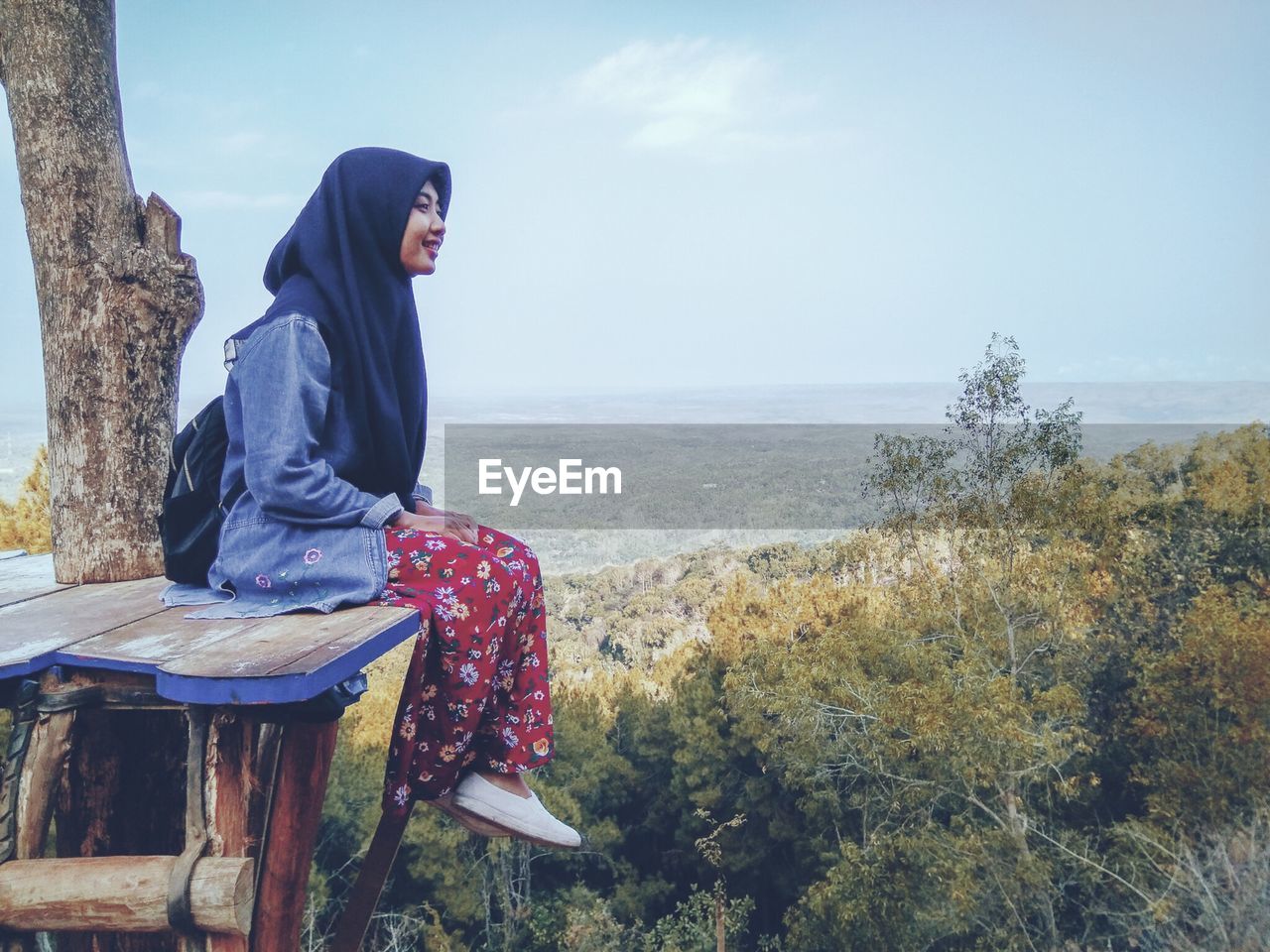 Side view of woman sitting on land against sky