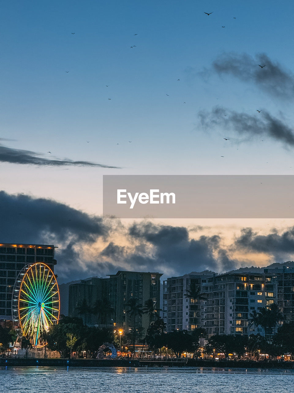 A city skyline with a ferris wheel in the background. the sky is cloudy and the sun is setting