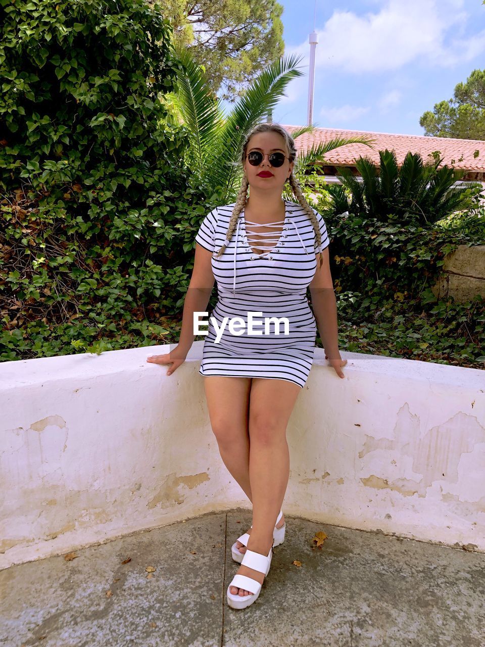 Portrait of young woman wearing sunglasses while standing against retaining wall