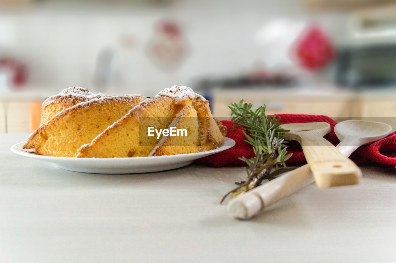 Close-up of christmas sponge cake on a kitchen table with wooden utensils and rosemary 