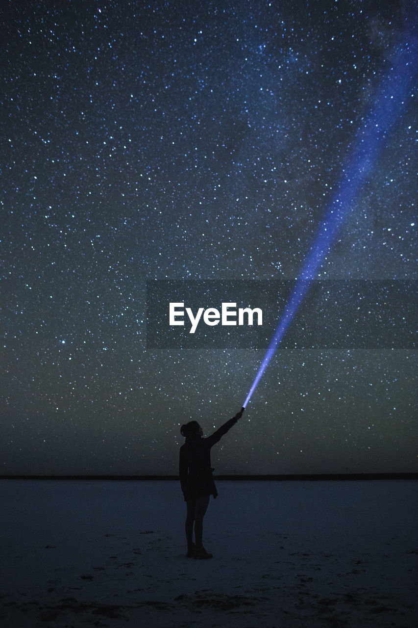 Full length of woman with flashlight standing against star field at night