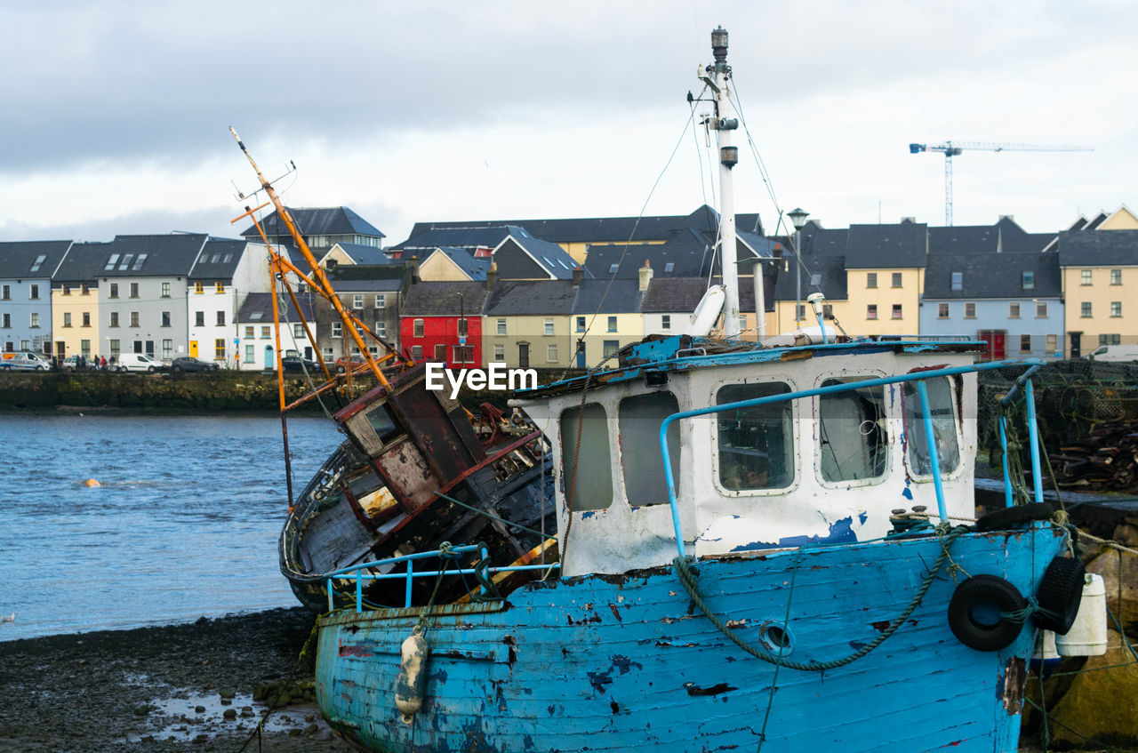 Fishing boats in sea by buildings against sky