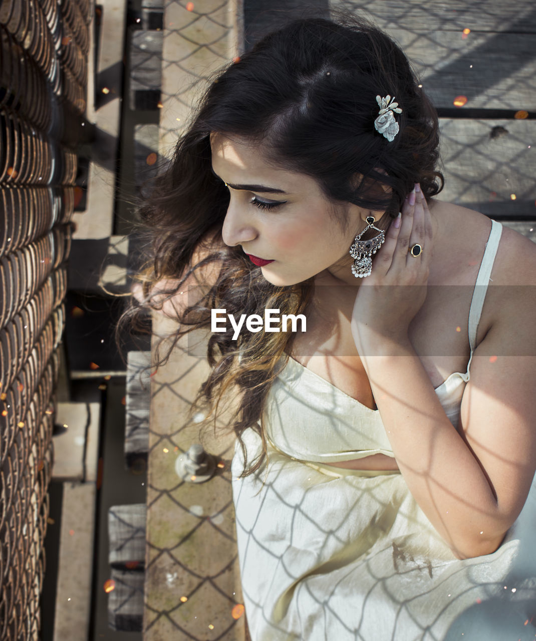 Beautiful woman looking away while sitting by chainlink fence