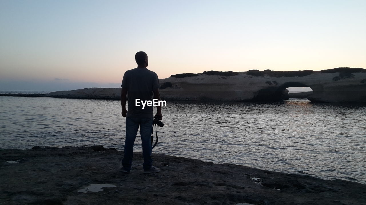 Rear view of man standing at beach against sky