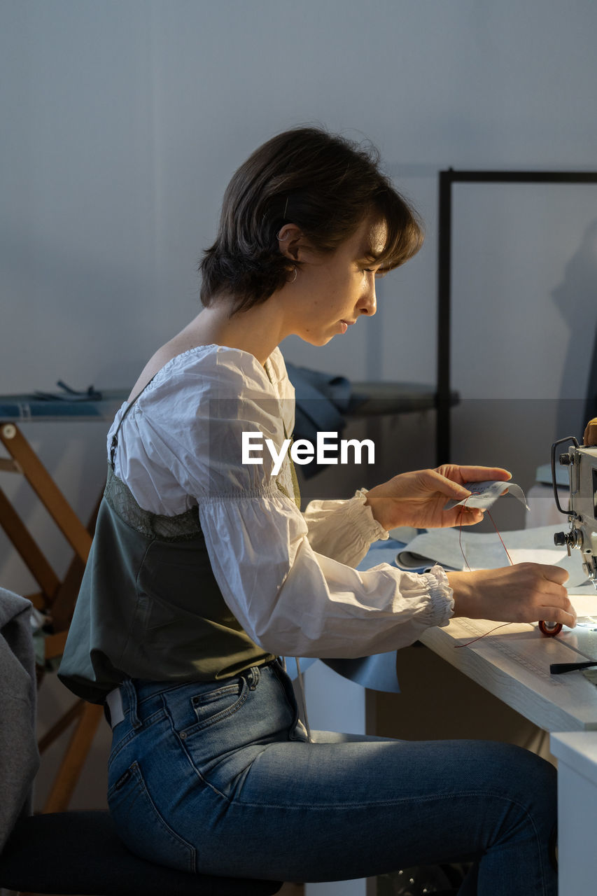 Young female seamstress sew on sewing machine, tailor sit at workplace in fashion workshop atelier