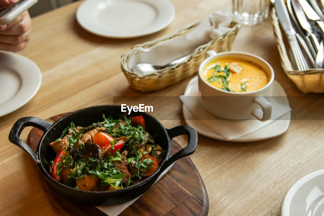 Black frying pan on a wooden plank served in a cafe, grilled meat with vegetables