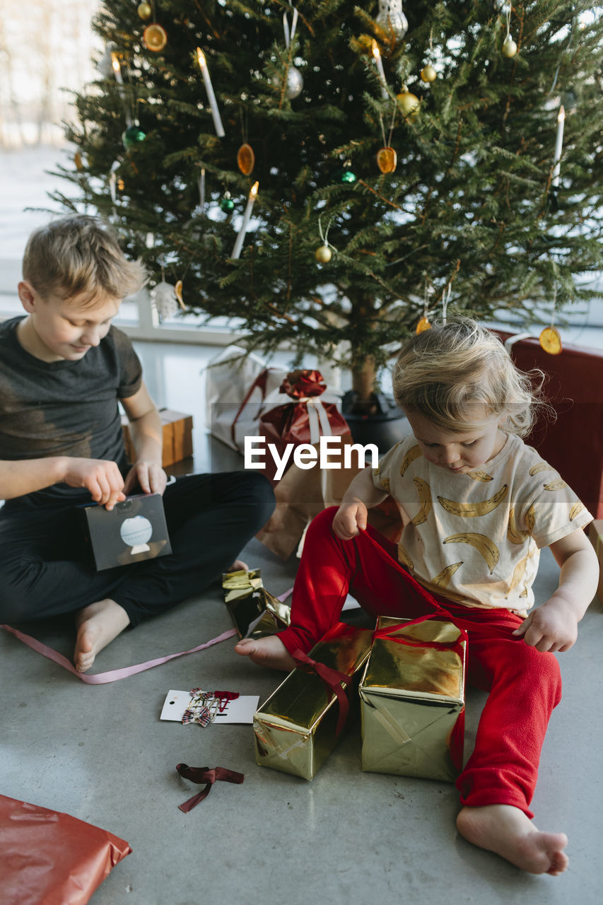Brother and sister opening christmas presents under christmas tree  barefoot