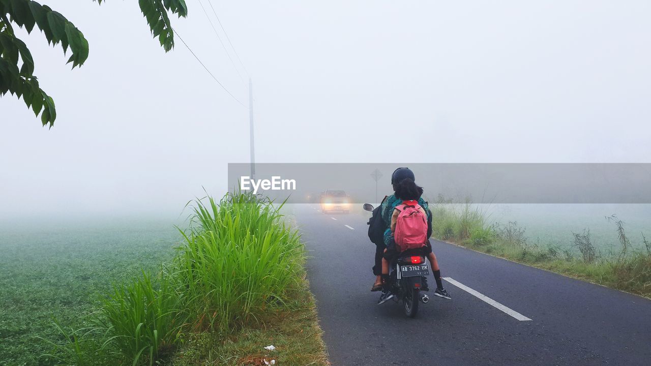 REAR VIEW OF MAN RIDING WOMAN ON ROAD