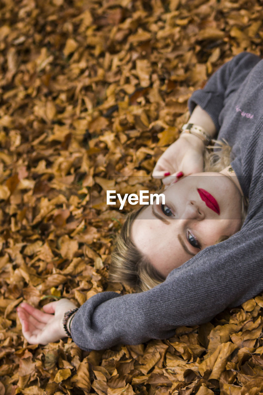 High angle portrait of woman lying down on autumn leaves