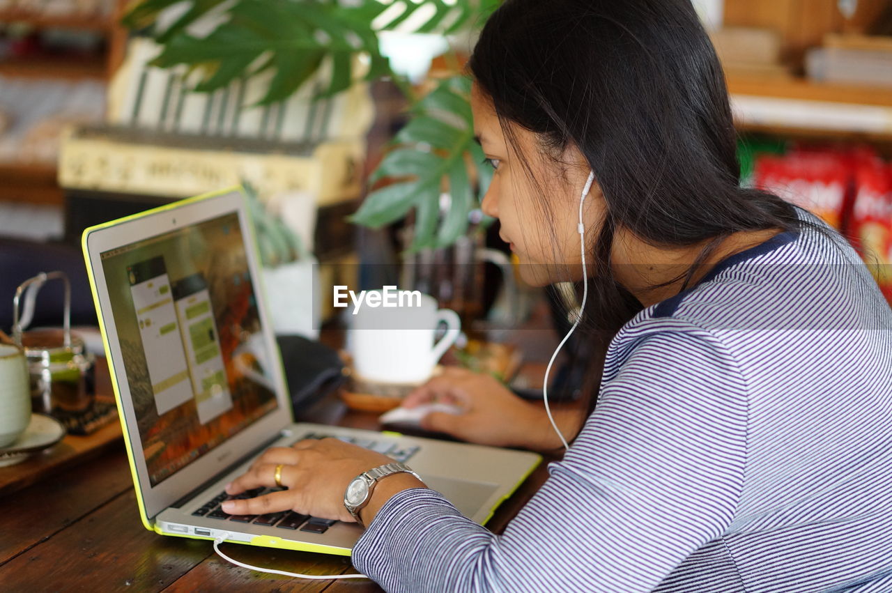 Side view of mid adult woman using laptop on table