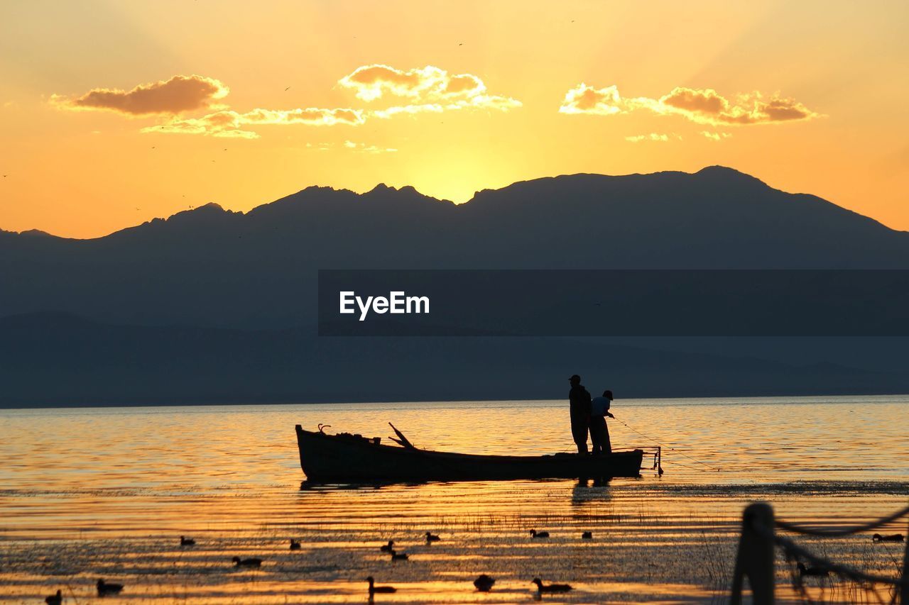 Silhouette man on boat at lake against sky during sunset