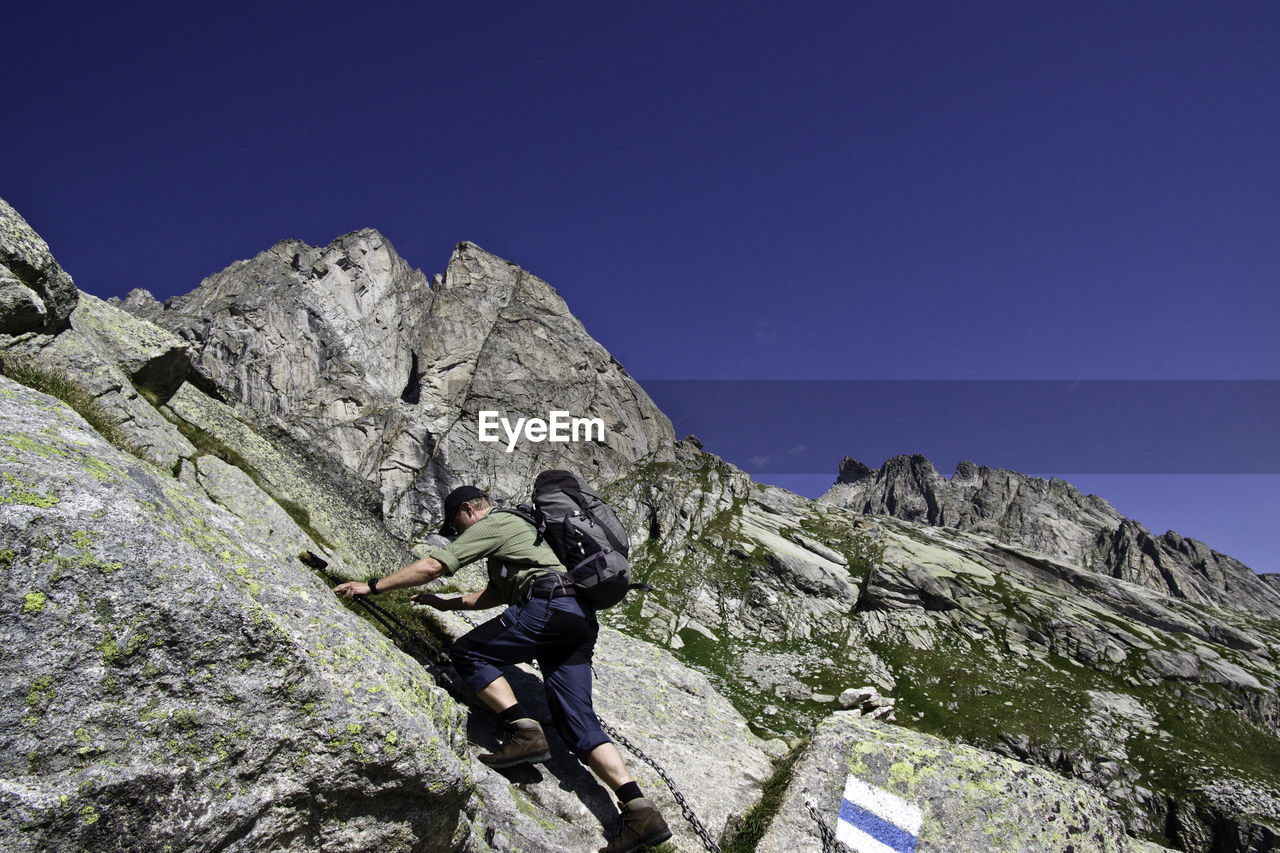 Low angle view of man climbing mountain against blue sky