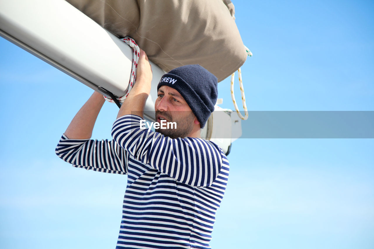 Low angle view of man holding canvas while standing against blue sky