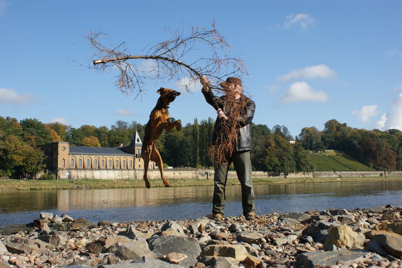 WOMAN STANDING ON RIVERBANK AGAINST SKY