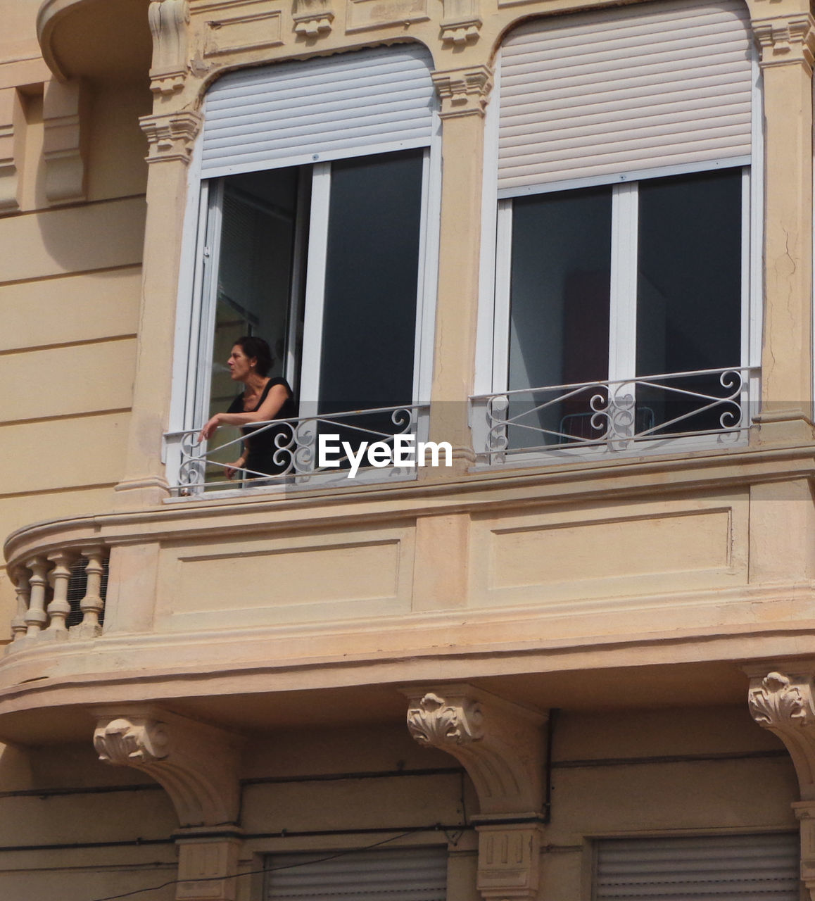 LOW ANGLE PORTRAIT OF WOMAN STANDING BY WINDOW AGAINST BUILDING