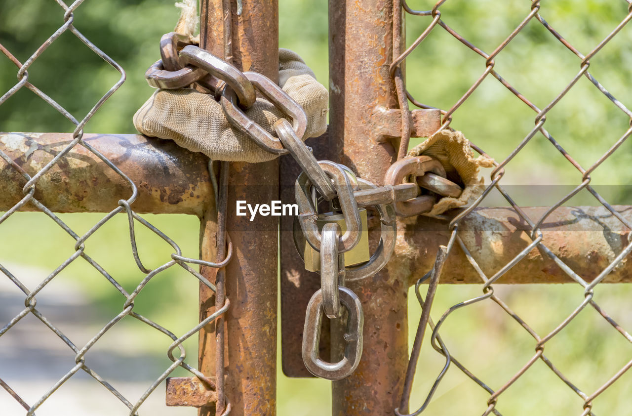CLOSE-UP OF RUSTY METAL FENCE WITH CHAIN AND GATE