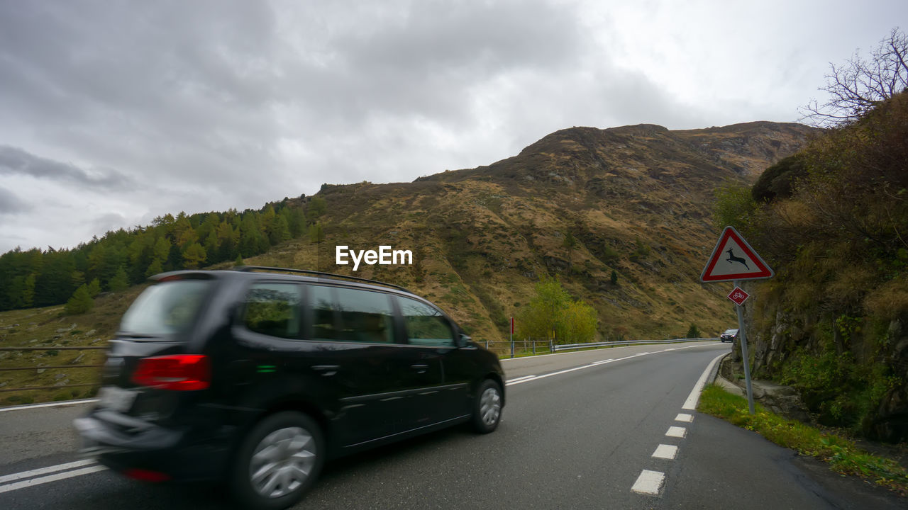 CAR ON ROAD AGAINST MOUNTAINS