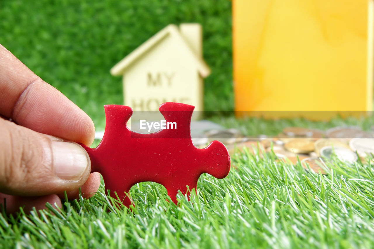 CLOSE-UP OF HAND HOLDING RED TOY WITH GRASS