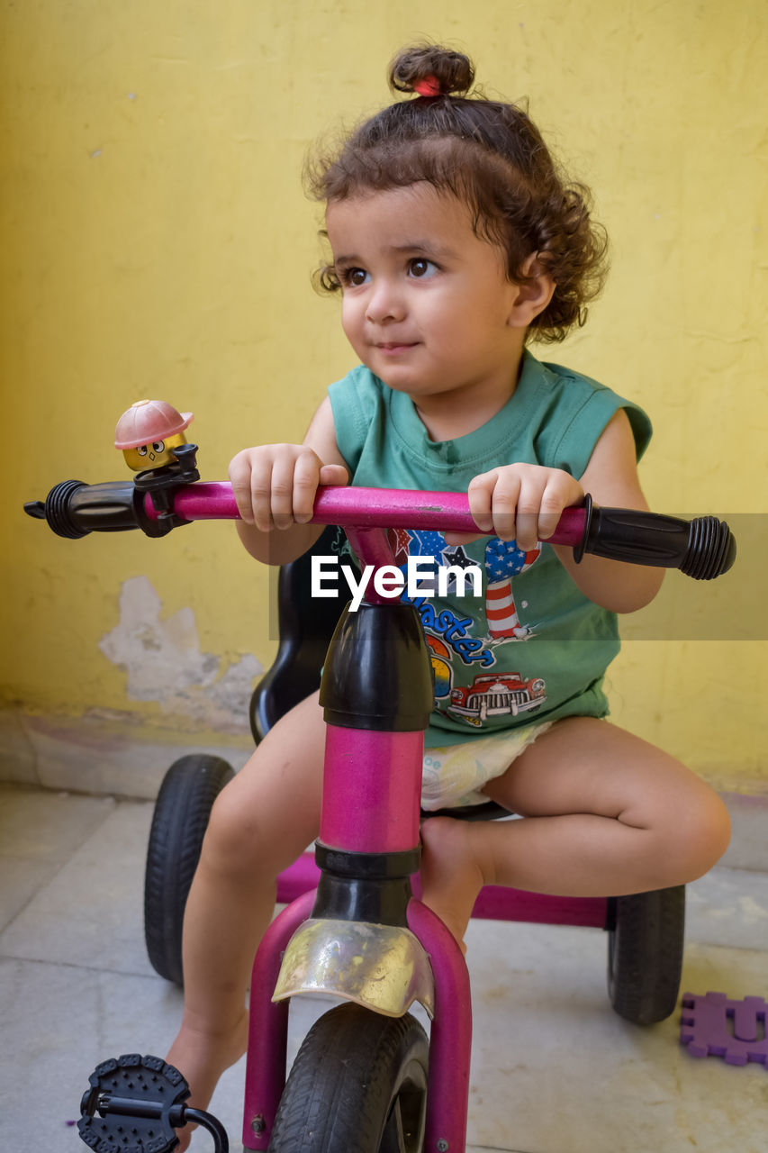 childhood, child, one person, bicycle, full length, tricycle, female, women, sitting, vehicle, toddler, land vehicle, lifestyles, portrait, cute, person, sports, footwear, leisure activity, looking at camera, innocence, holding, clothing, training wheels, cycling, front view, casual clothing, smiling, activity, wheel, fun, tire, riding, toy, sports equipment, brown hair, emotion