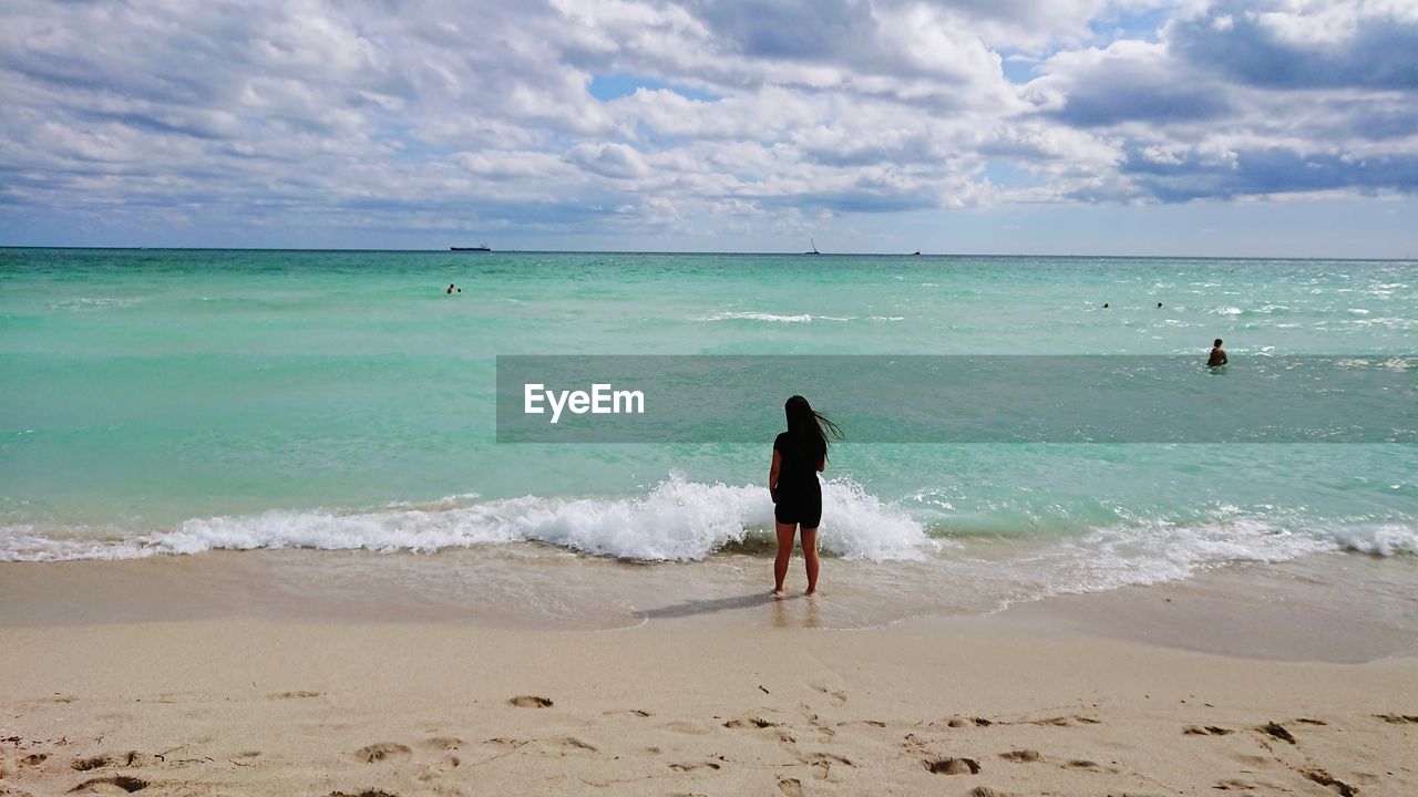 Rear view of woman on beach against sky