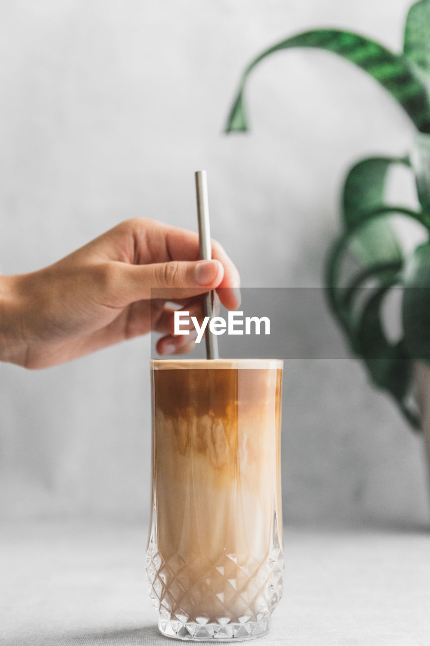 Midsection of person holding metal straw in iced coffee drink on table