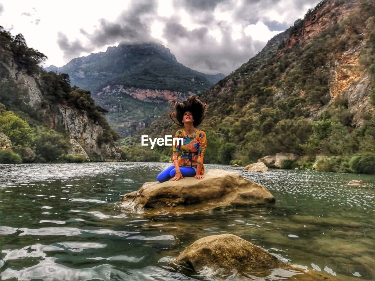 Woman tossing hair while sitting on rock amidst lake