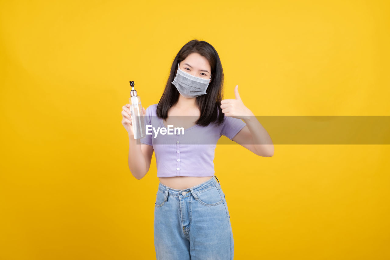 PORTRAIT OF BEAUTIFUL YOUNG WOMAN STANDING ON YELLOW BACKGROUND