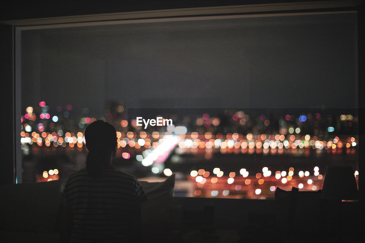 Rear view of woman looking at illuminated city through window