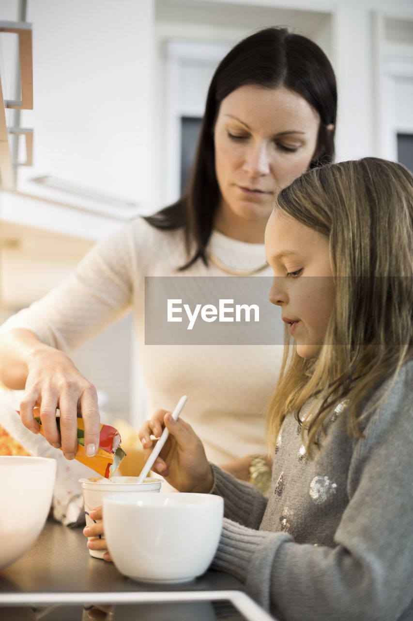 Mother and daughter adding flavor in cup at kitchen