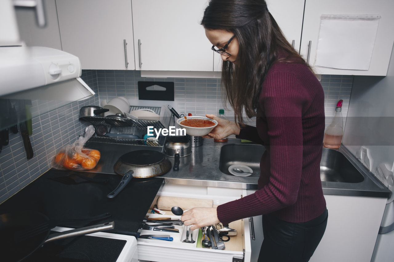 Side view of woman picking spoon from drawer in kitchen