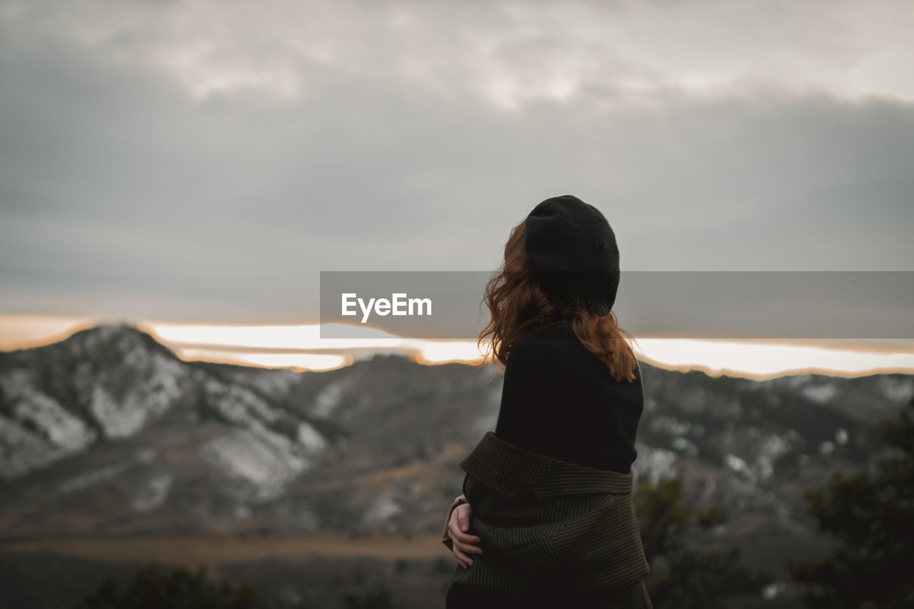 Young woman with her back turned looking at the rocky mountain foothills at sunset. 