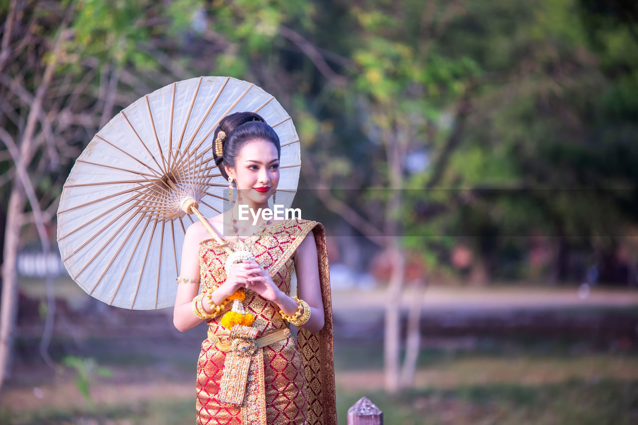 Beautiful woman in traditional clothing looking away while holding paper umbrella