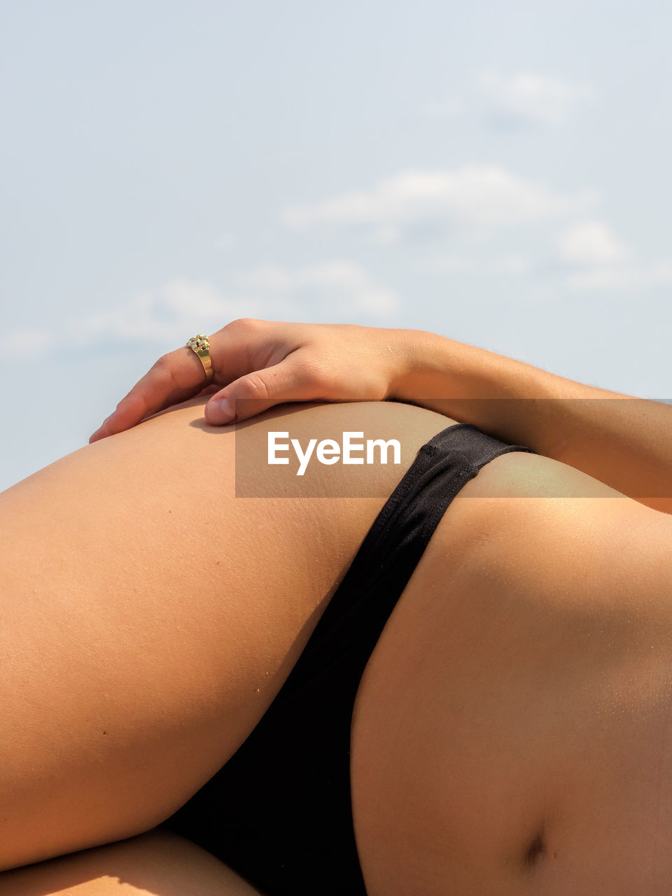 Midsection of woman wearing bikini bottom lying against sky on sunny day