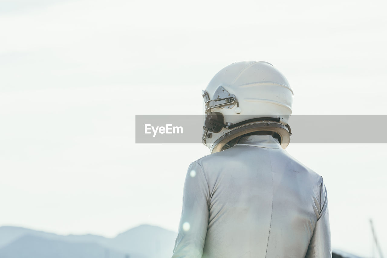 Back view man in spacesuit and helmet looking away while standing on path on sunny day in nature