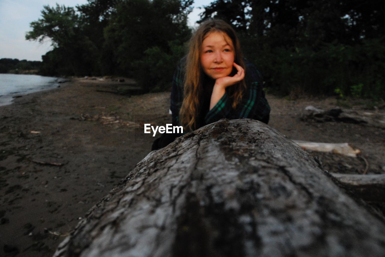 Smiling woman sitting by driftwood at beach