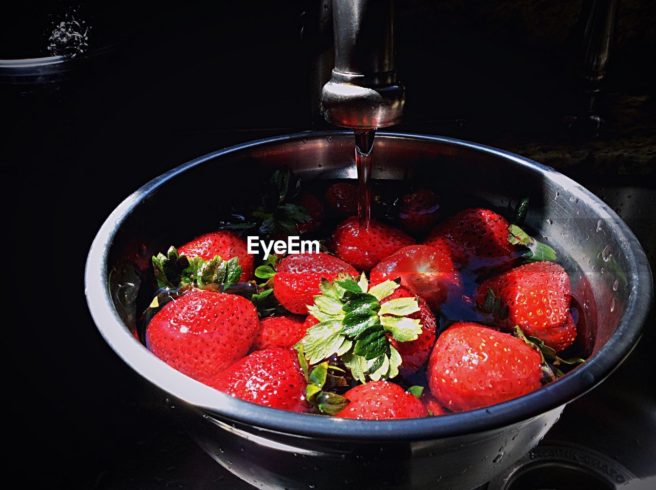 Faucet pouring water in strawberry bowl