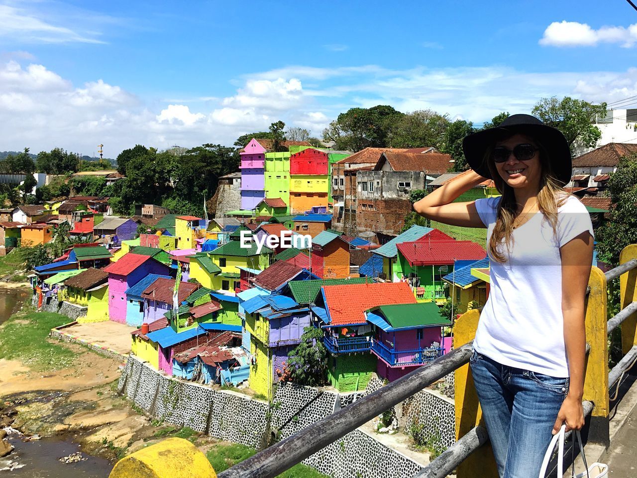 Woman wearing hat standing against colorful houses during sunny day