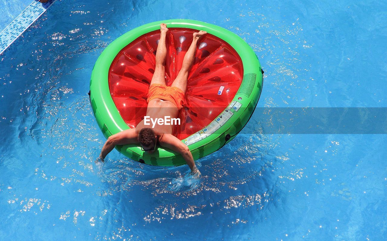 High angle view of shirtless man with pool raft floating on swimming pool