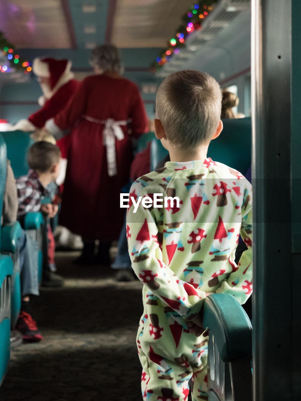 Rear view of boy looking at people dressed as santa claus in train