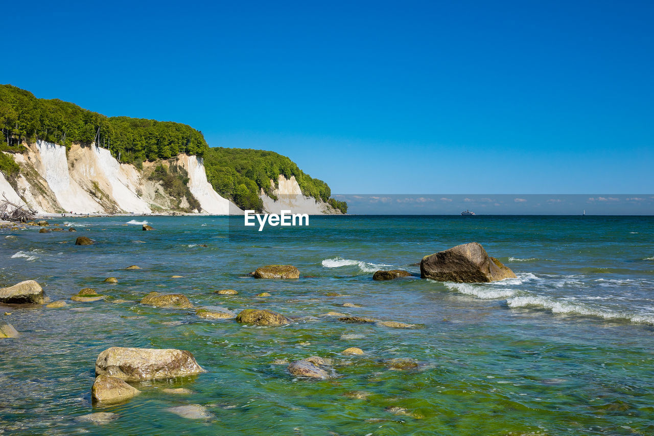 Scenic view of sea and rock formations against clear blue sky