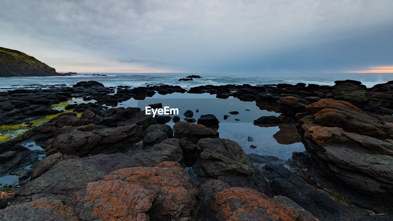 Rocks on beach against sky during sunset